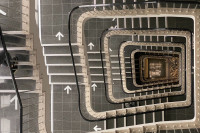 Blick von oben auf ein graues Treppenhaus mit weißen Pfeilen, die nach oben weisen